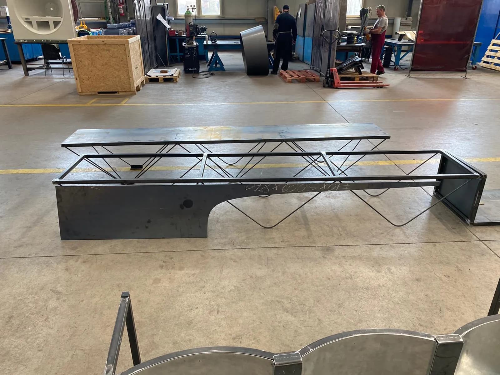 A low steel platform on rod legs next to a seat module with an arched cut-out, in the production hall