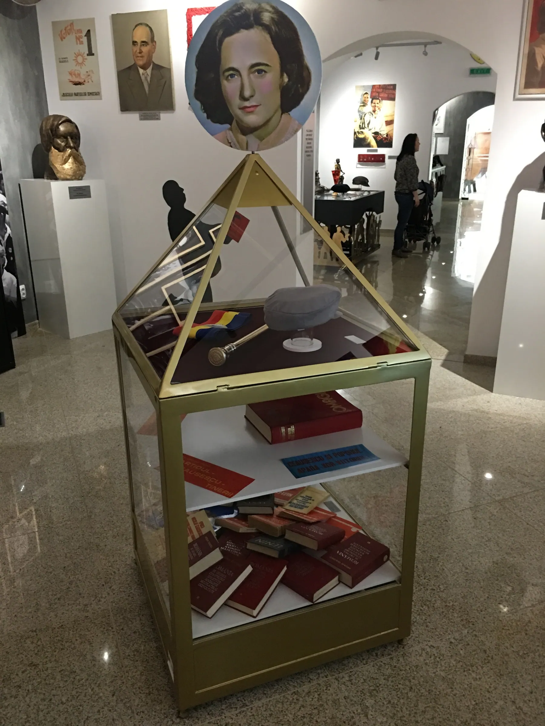 Gold pyramid-shaped display case with books on its shelves, in the museum hall
