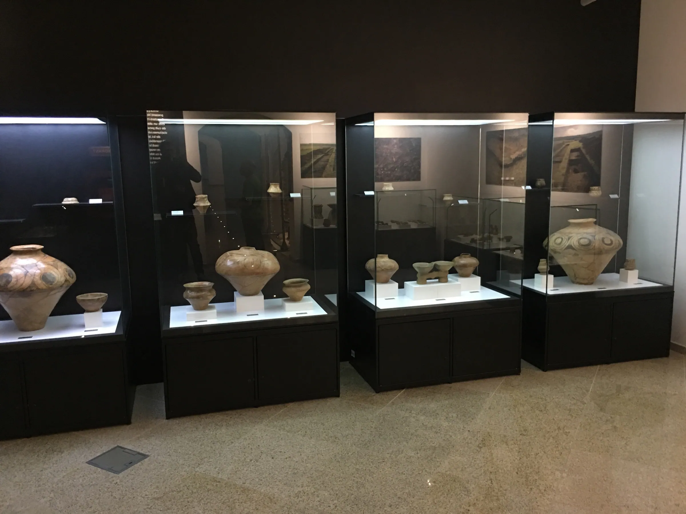 A row of lit display cases with painted pottery on black plinths
