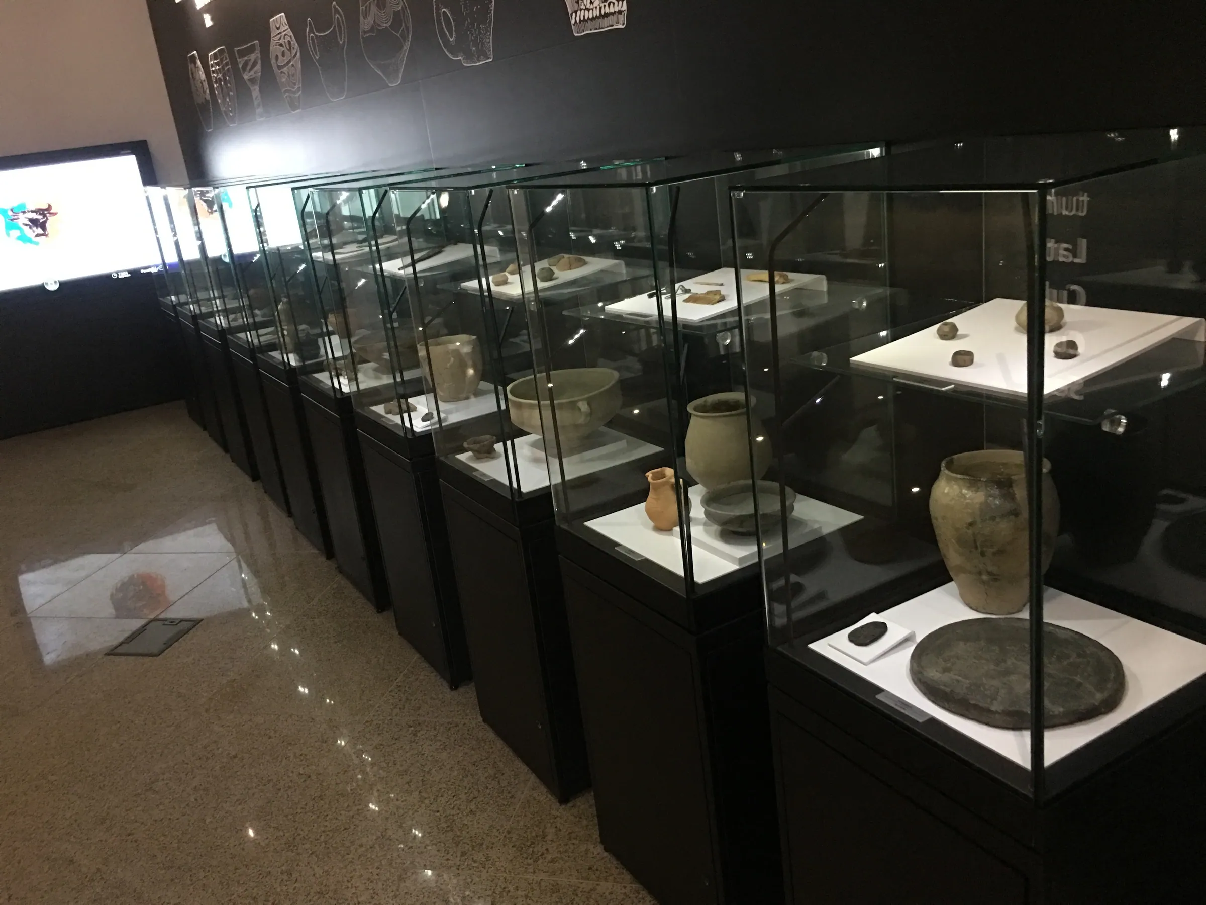 Glass display cases lined up along the hall, with vessels and archaeological objects